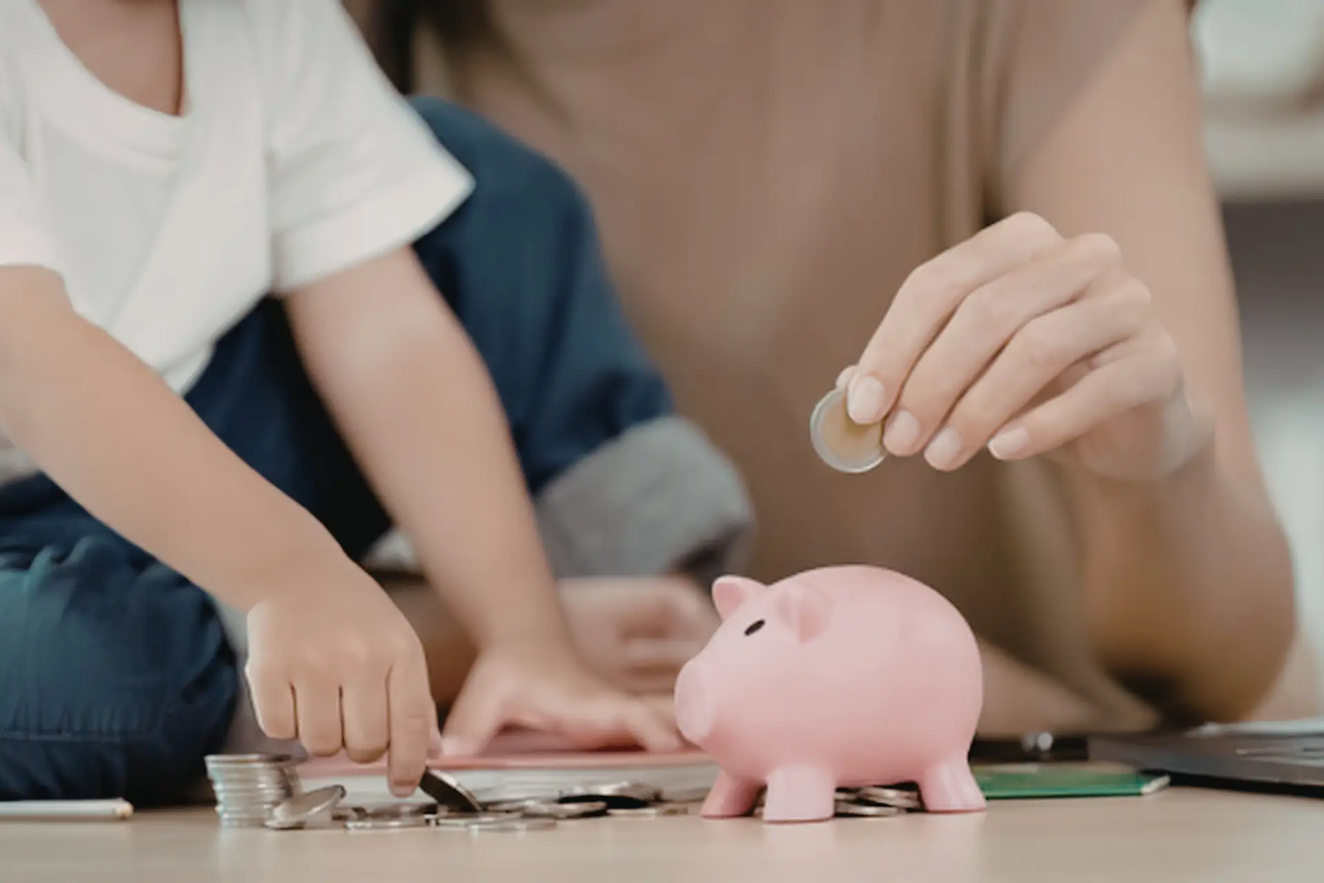 child and adult sit next to each putting coins in a piggy bank